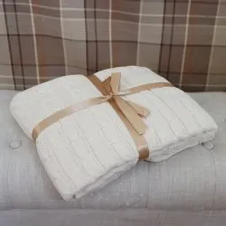 Beige kabelstickad pläd, vikt på ljus soffa